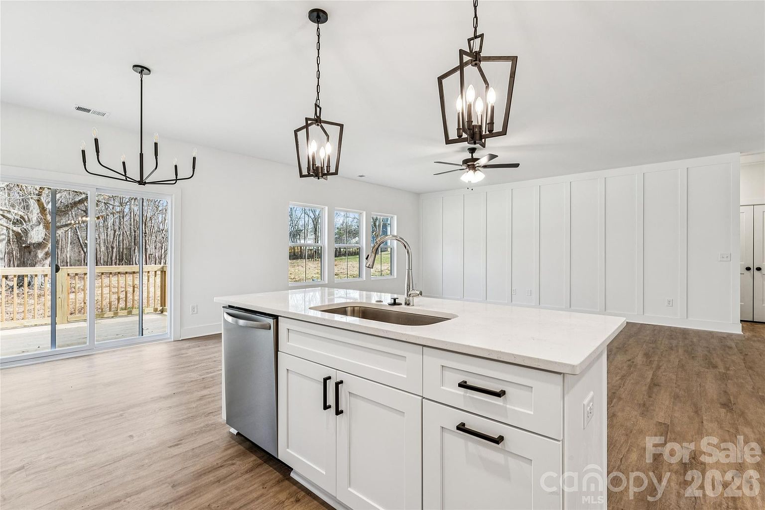 Wide view of the kitchen island with quartz top, ceiling fan in the adjacent great room, and sliding door to the rear deck