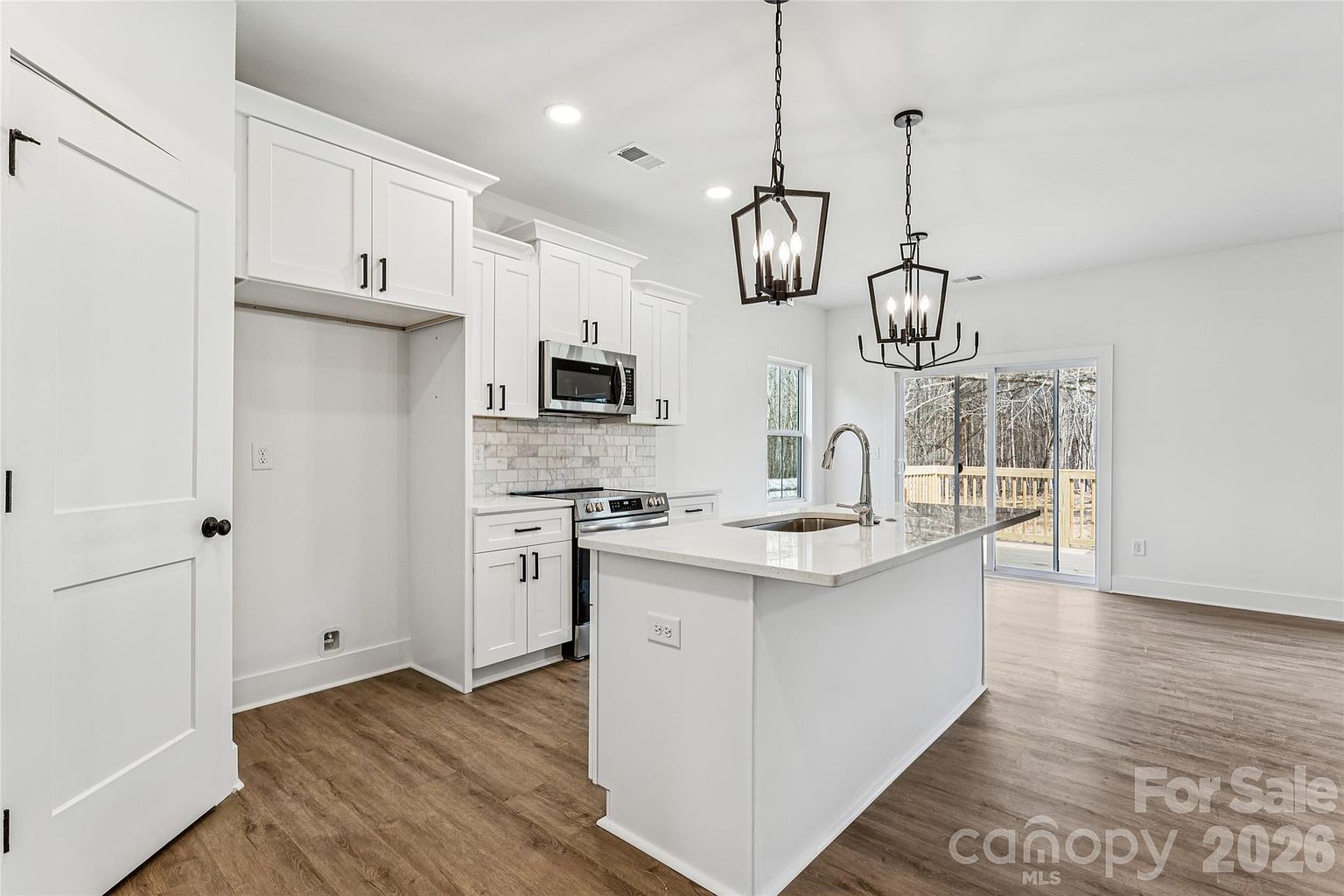Full kitchen view with white cabinetry, pantry door, stainless range and microwave, and island overlooking the dining area