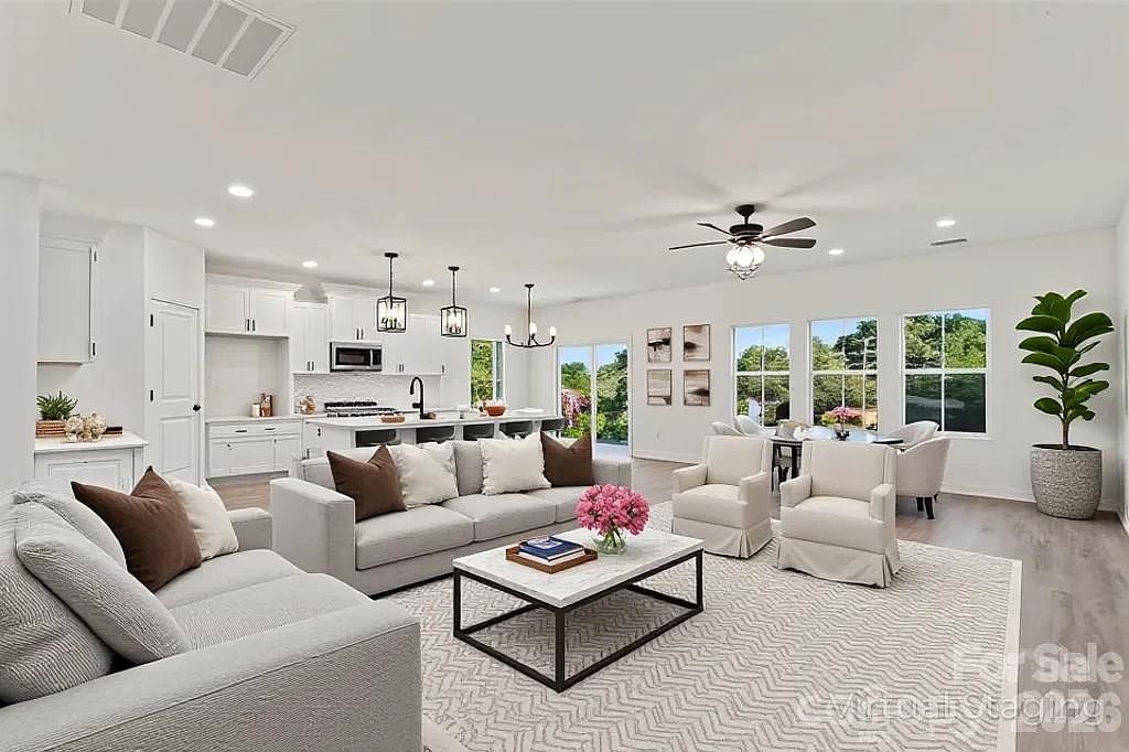 Bright open-concept living room with comfortable seating, ceiling fan, and views into the modern white kitchen