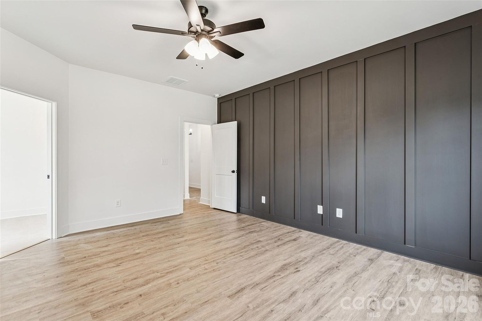Primary bedroom from a second angle showing the dark accent wall, ceiling fan, and open doorway to the en-suite bathroom