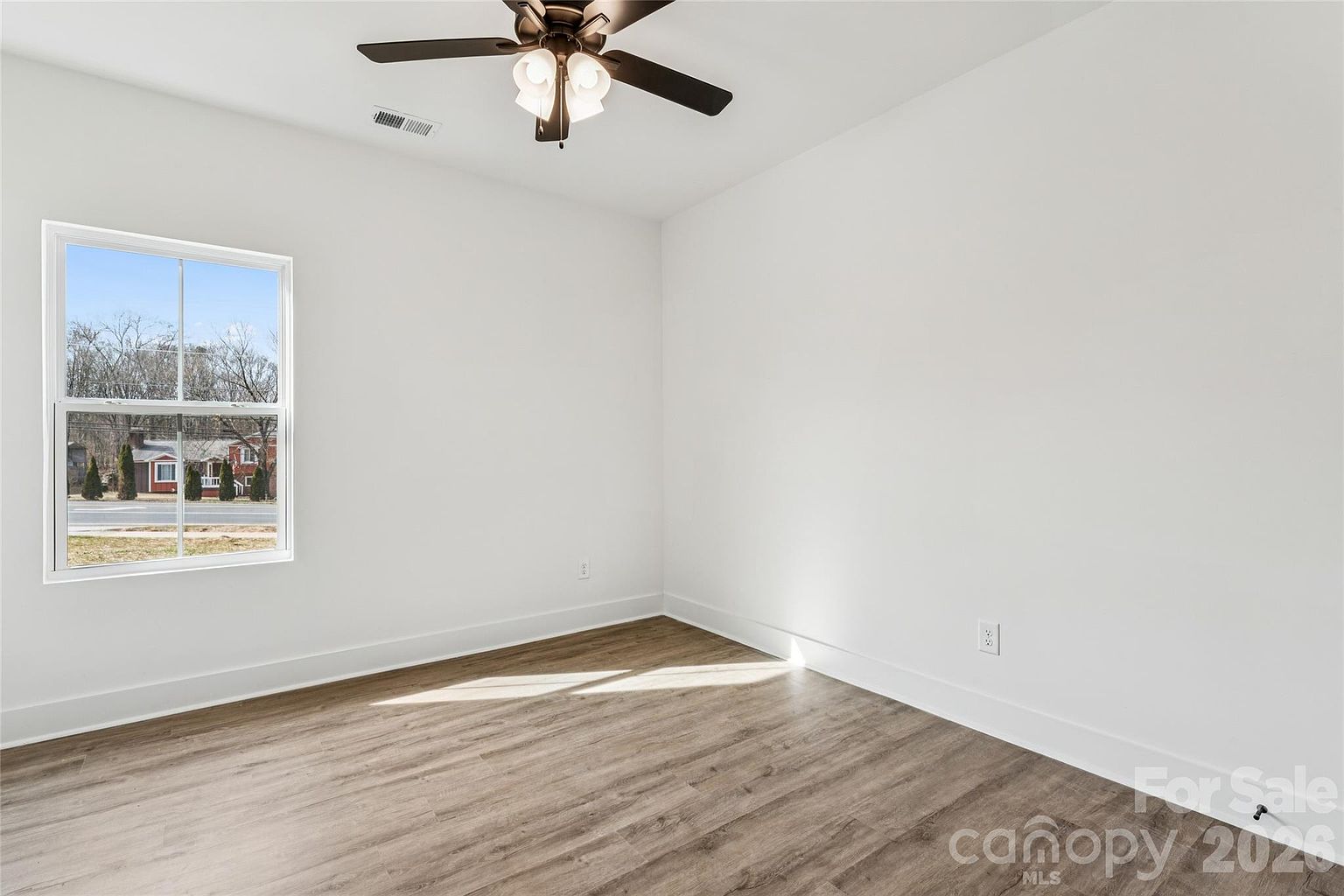Sunny bedroom with ceiling fan and a large window with afternoon light and a view of the street