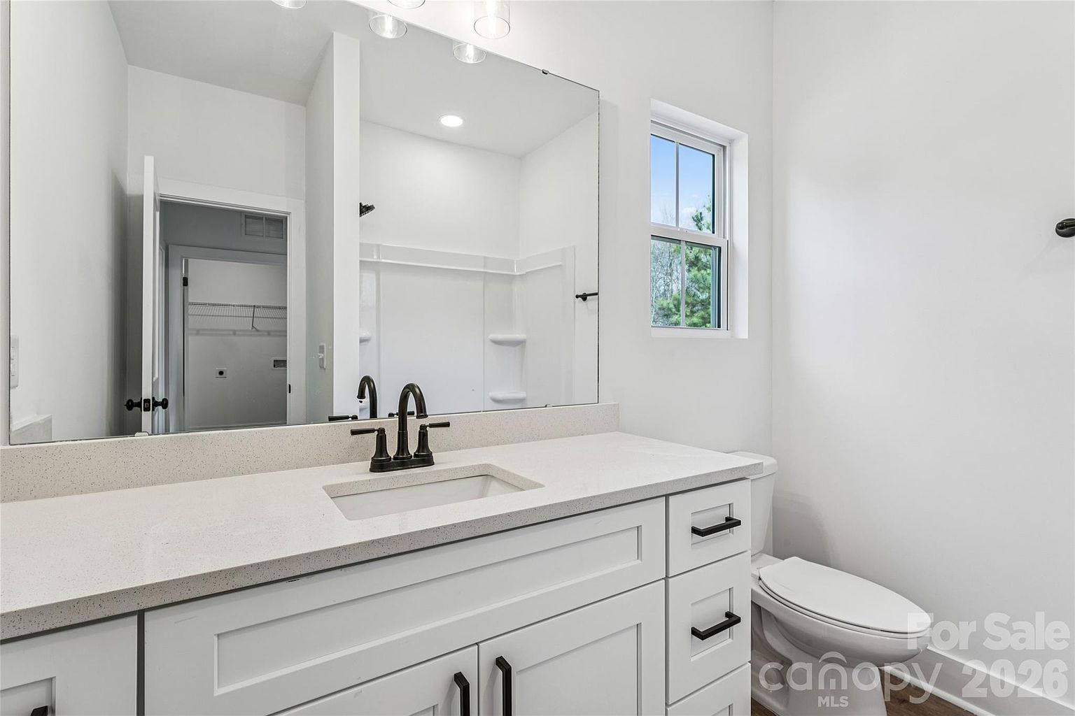 Guest bathroom with single vanity, quartz countertop, large mirror, and tub-shower combination visible in the reflection