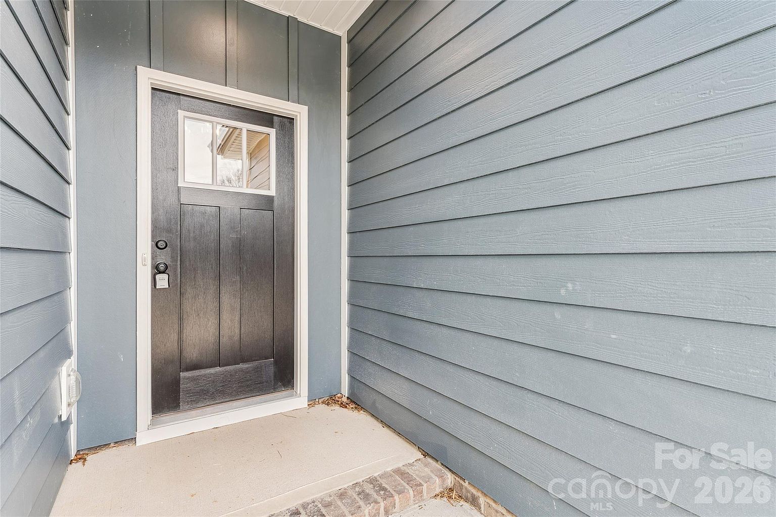 Covered front entry with black craftsman-style door and glass panel set against blue-gray siding